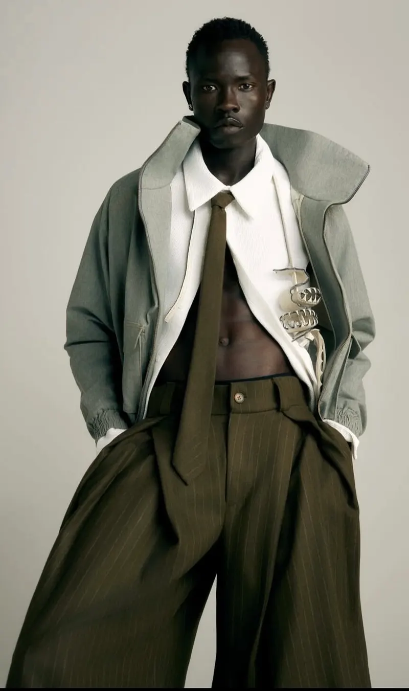 Studio portrait of a model in a grey jacket, white shirt, olive tie and wide pinstripe trousers