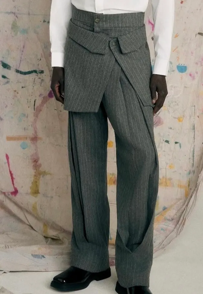 Detail of grey pinstripe trousers with a folded waistband, against a paint-splattered backdrop